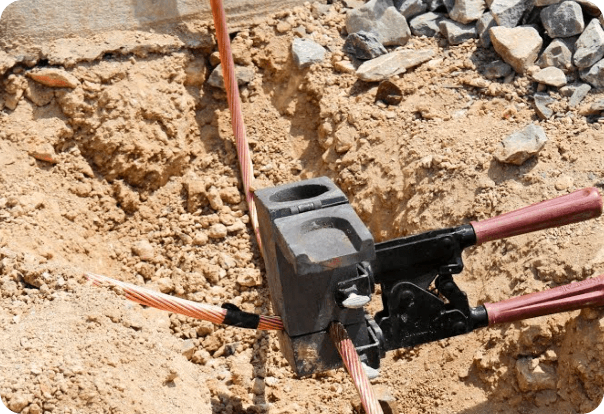Electrical wires being connected using a crimping tool in a trench.